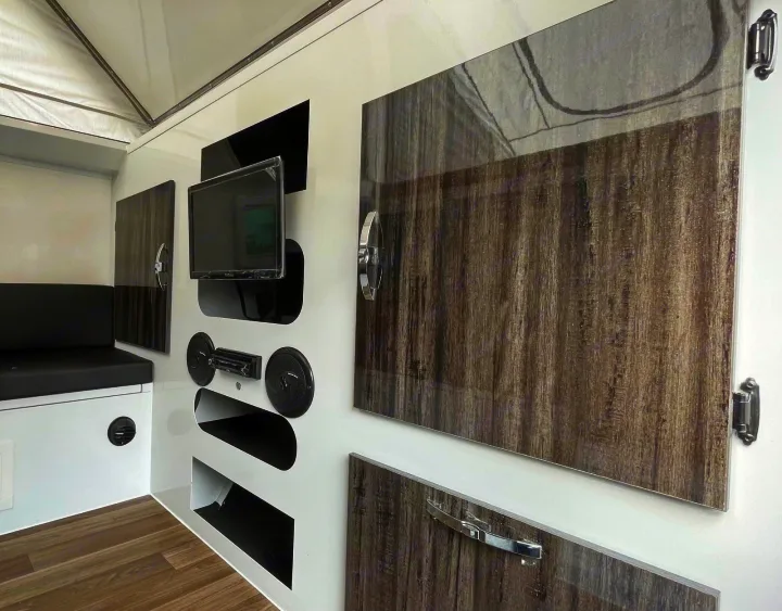 Modern RV rental interior showing a TV, audio system, bench seating, and wood-grain cabinets for a comfortable journey.. Zoomies Campers Spirit 2025