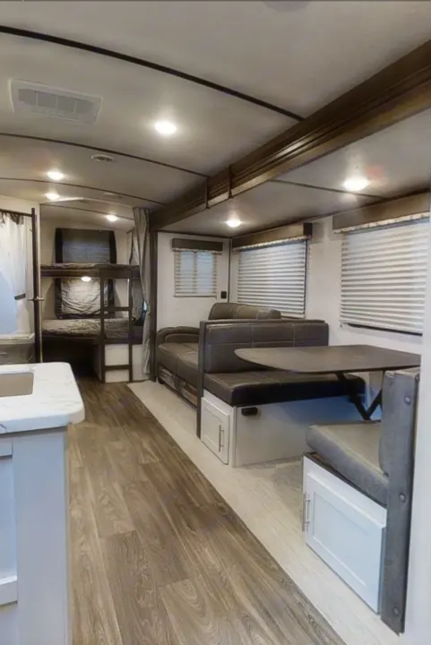 Spacious RV rental interior featuring bunk beds, a dinette, sofa, and kitchen counter with wood flooring.. Keystone RV Bullet Ultra Lite 2021