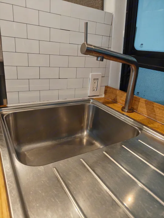 Compact RV rental kitchen featuring a stainless steel sink, modern faucet, subway tile backsplash, and wooden countertop.. Mercedes-Benz Sprinter 2017