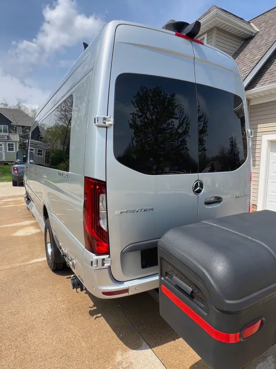 A sleek silver Mercedes-Benz Sprinter van, an ideal RV rental, is parked outdoors with a rear-mounted StowAway cargo box.. Ultimate Toys Ultimate Coach 2024