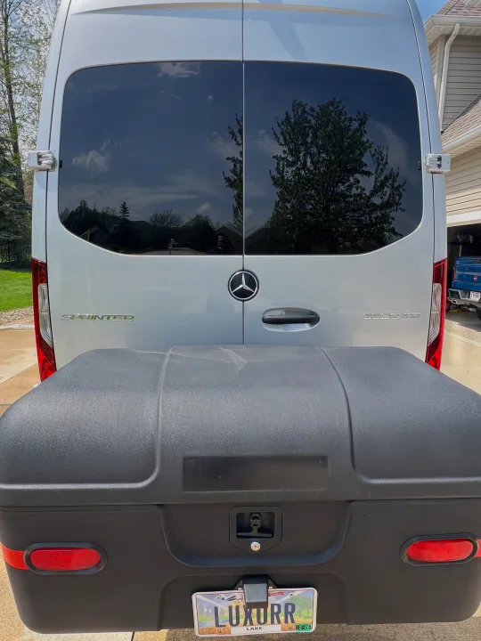 Rear of silver Mercedes Sprinter van with large black cargo box & custom 'LUXURR' plate. An excellent rv rental option.. Ultimate Toys Ultimate Coach 2024