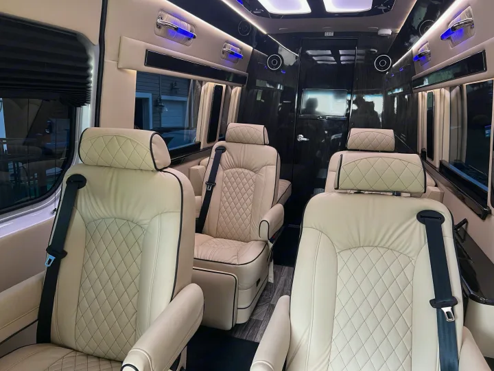 Inside a luxury rv rental: plush cream quilted seats with black trim, blue accent lights, and sleek dark paneling create a lavish cabin.. Ultimate Toys Ultimate Coach 2024
