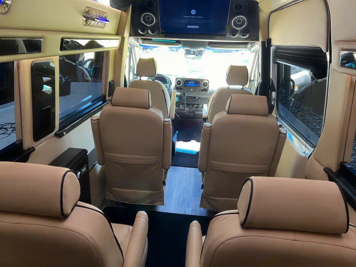 View inside a spacious RV rental, showcasing tan leather captain's chairs, a front TV, and wood-grain accents for luxury travel.. Ultimate Toys Ultimate Coach 2024