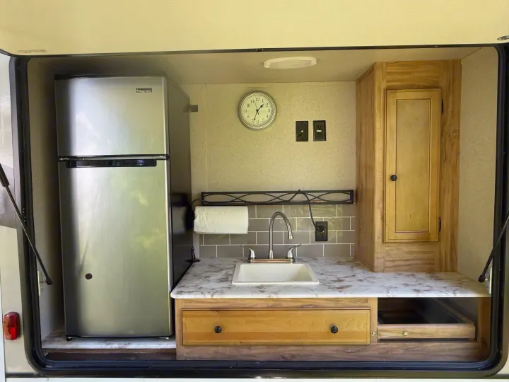 An RV rental's outdoor kitchen featuring a Magic Chef refrigerator, sink, cabinet, and drawer storage.. Coachmen Freedom Express Ultra Lite Maple Leaf Edition 2019