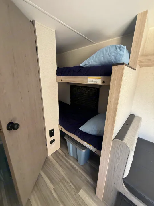 Comfortable bunk beds within an rv rental, featuring navy mattresses, light wood frames, storage, & dinette area.. Heartland Pioneer 2025
