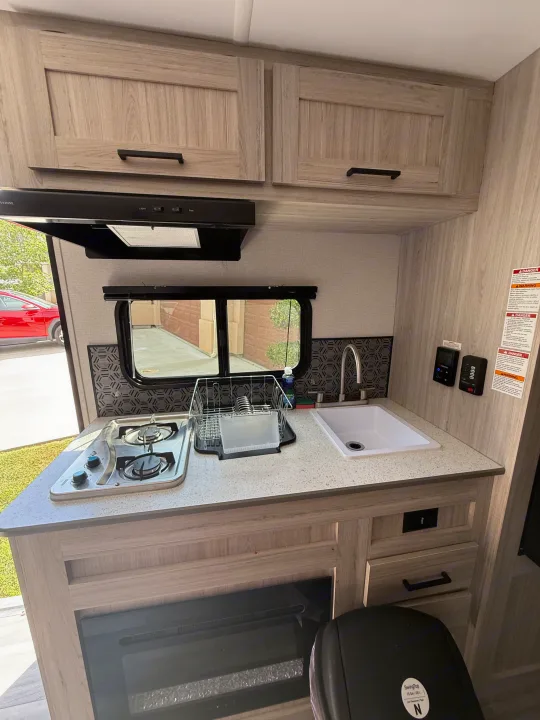 RV rental kitchen showcasing a two-burner stovetop, sink, and wood-look cabinets. Ideal for road trip cooking.. Heartland Pioneer 2025