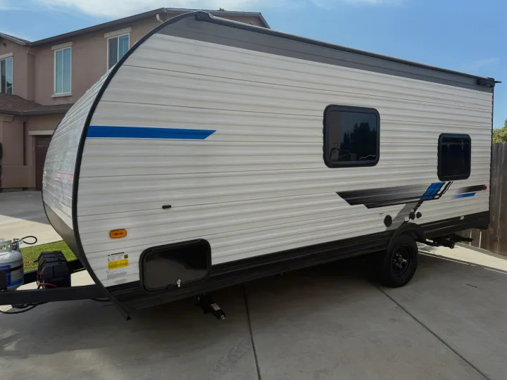 Clean white travel trailer for RV rental, with blue decals, parked in a sunny residential driveway.. Heartland Pioneer 2025