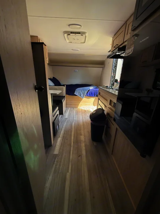 Bright rv rental interior, with wood-look floors, a bed, dinette, & kitchen area, seen from the entrance.. Heartland Pioneer 2025