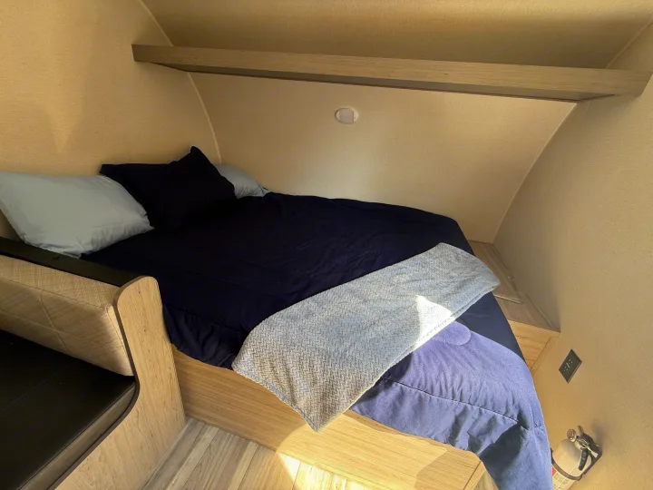 RV rental bedroom with a cozy bed, blue bedding, overhead shelf, bench, and fire extinguisher for safety.. Heartland Pioneer 2025