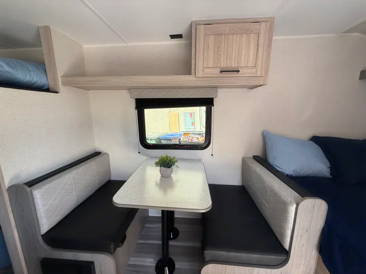 Inside an RV rental: a cozy dinette with dual benches, a table, overhead storage, and an upper bunk bed.. Heartland Pioneer 2025