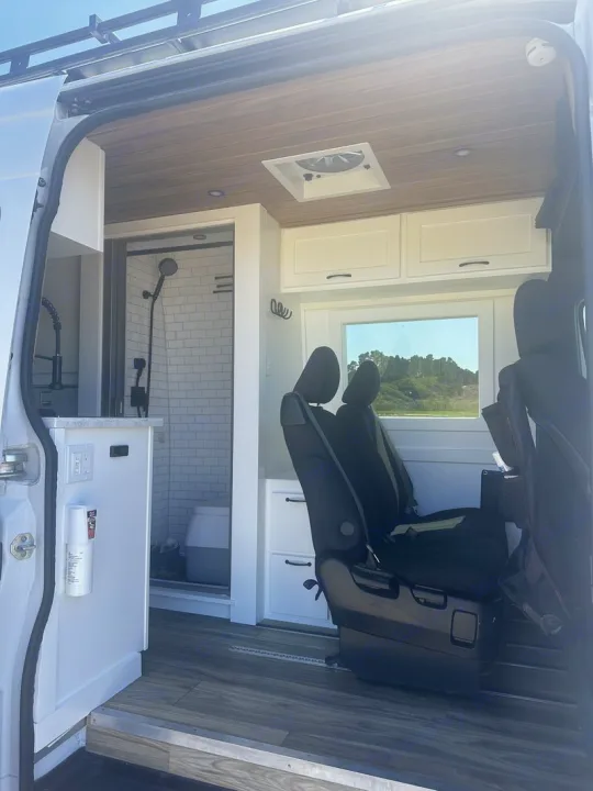 Inside a modern RV rental: full shower, kitchen, and comfortable seating in a custom camper van.. Custom Crafted Vans Family Van 2019