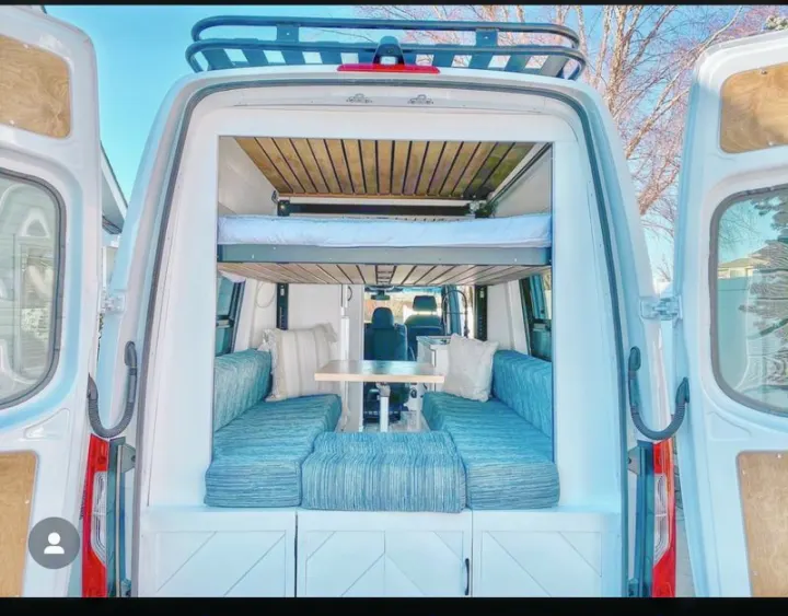 This custom camper van interior, perfect for rv rental, features a clever layout with an elevated bed over comfy seating and dining.. Custom Crafted Vans Family Van 2019