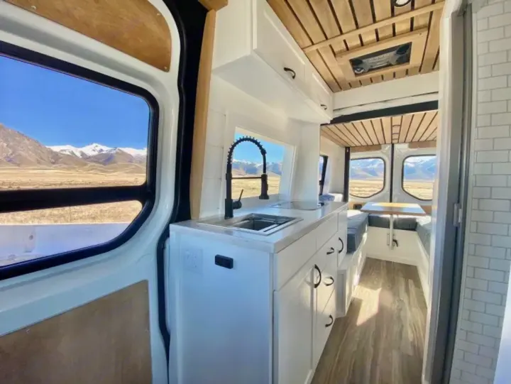 This RV rental offers a modern camper van interior with a kitchen, dining, and scenic mountain views.. Custom Crafted Vans Family Van 2019