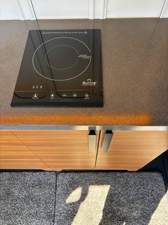 Top-down view of an RV rental kitchen showing a modern duxTop induction cooktop on a gray speckled counter.. Ford Transit 2022