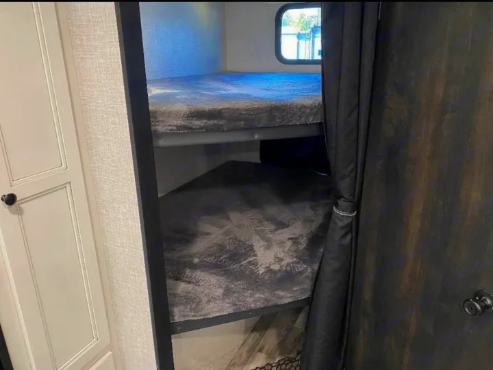 This RV rental features a cozy sleeping area with two bunk beds and privacy curtains.. Highland Ridge RV Range Lite 2023