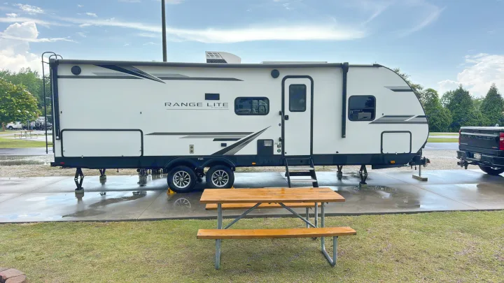 A bright white RV rental, a Range Lite by Highland Ridge, parked on a wet concrete pad at a scenic campground. Perfect for travel!. Highland Ridge RV Range Lite 2023