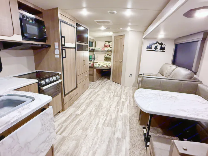 Explore this RV rental's inviting interior, featuring a full kitchen, bunk beds, and cozy living space.. Grand Design Imagine 2021