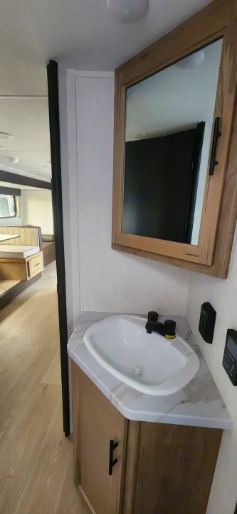 Inside an RV rental: Compact bathroom with a modern sink, vanity, and mirror, leading to a bright dinette area.. Forest River Cherokee Grey Wolf 2026