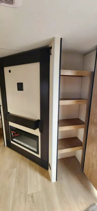Modern RV rental interior with an electric fireplace, TV mount, and built-in shelving for compact living.. Forest River Cherokee Grey Wolf 2026
