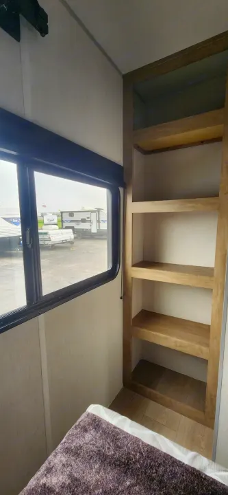 Interior view of an RV rental, featuring a cozy bed, a window looking out onto a lot, and built-in storage shelves.. Forest River Cherokee Grey Wolf 2026