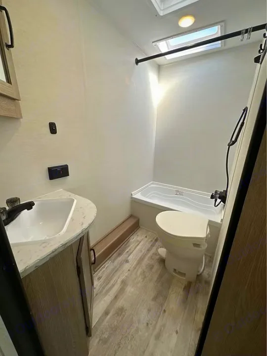 Compact RV rental bathroom featuring a small vanity, toilet, and mini tub/shower combo with a skylight.. Gulf Stream Amerilite 2025