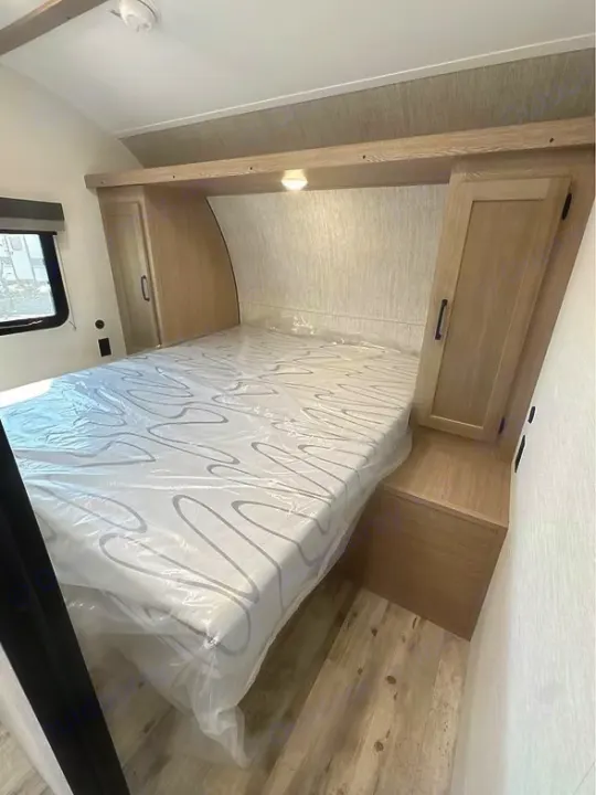 Clean RV bedroom interior showcasing a new, plastic-wrapped mattress, built-in storage, and light wood flooring. Great for an rv rental.. Gulf Stream Amerilite 2025
