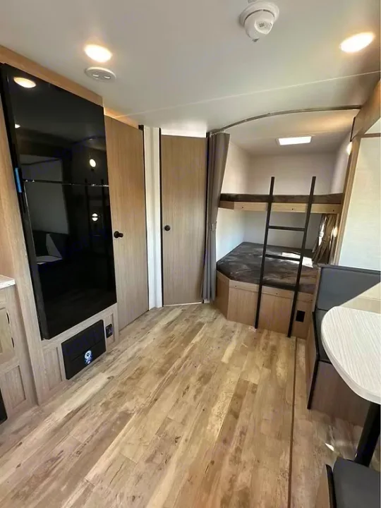Bright RV rental interior showcasing bunk beds, a dinette, and TV setup on wood-look flooring. Ready for your trip!. Gulf Stream Amerilite 2025
