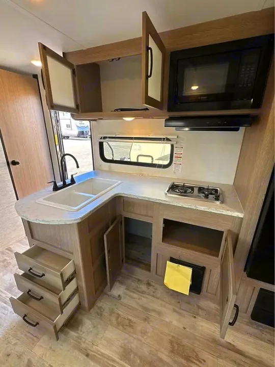 RV rental kitchen showing open cabinets, drawers, microwave, sink, and two-burner stove.. Gulf Stream Amerilite 2025