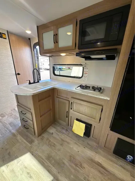 Step inside this sleek rv rental kitchen with light wood cabinetry, microwave, 2-burner stovetop, and sink.. Gulf Stream Amerilite 2025