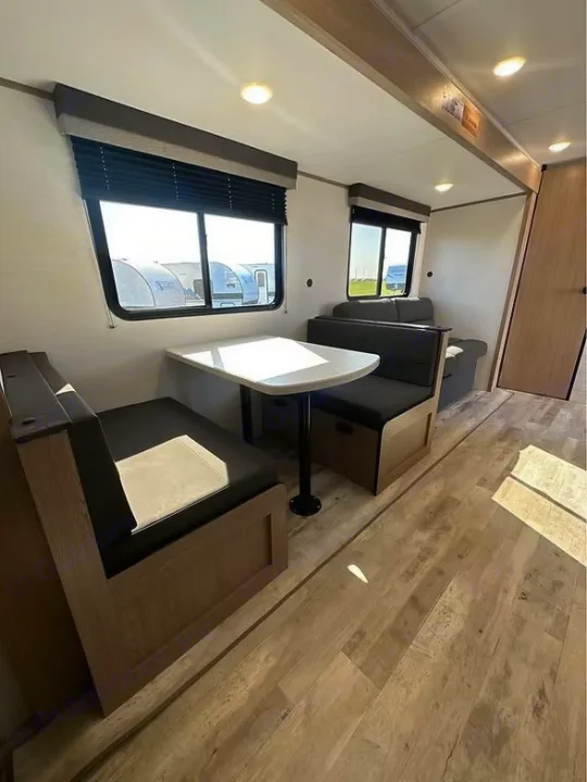 RV rental interior: Spacious camper dinette and living area with light wood finishes and dark upholstery.. Gulf Stream Amerilite 2025