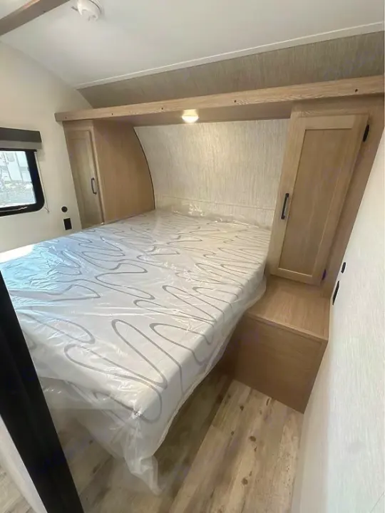 Clean RV rental bedroom featuring a plastic-covered mattress, side wardrobes, and overhead storage. Ready for travel.. Gulf Stream Amerilite 2025