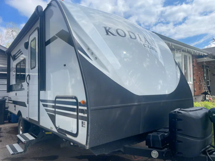 A sleek white and black Kodiak Cub travel trailer, ready for your RV rental, is parked outdoors in daylight next to a house.. Dutchmen Kodiak Cub 2021