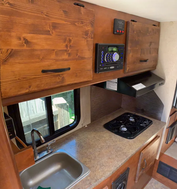 RV rental interior shows a functional kitchen with a two-burner stove, sink, and wood cabinetry, ideal for travel.. RAM 3500HD 2016