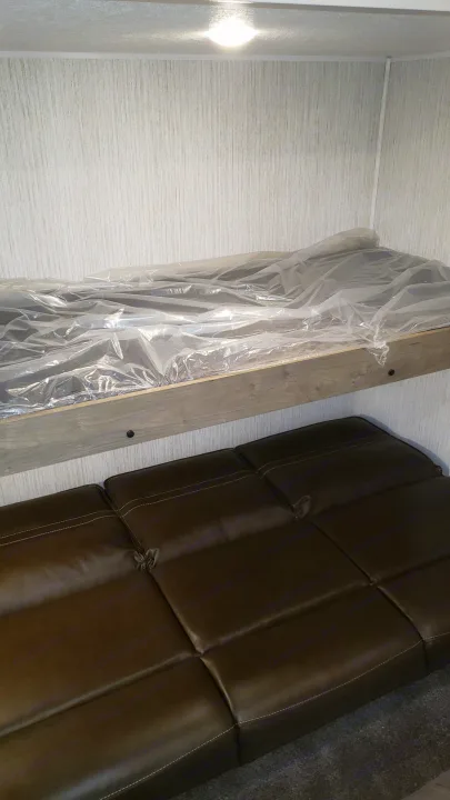 RV rental bunk beds, mattress still in plastic, and a brown sofa below. A compact, bright interior for your trip.. Palomino 32BHQS 2022