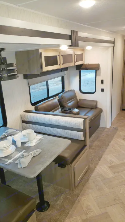 Explore this RV rental's modern interior featuring a dining booth, comfy sofa, windows, and overhead cabinets.. Palomino 32BHQS 2022