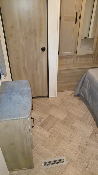 Inside an RV rental: detailed view of herringbone wood flooring, light wood cabinets, and a bed area. Practical and stylish RV living.. Palomino 32BHQS 2022