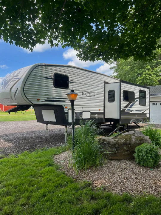 A white Puma fifth-wheel RV is parked on gravel, amidst green landscaping; perfect for an rv rental trip.. Forest River Palomino Puma 2022