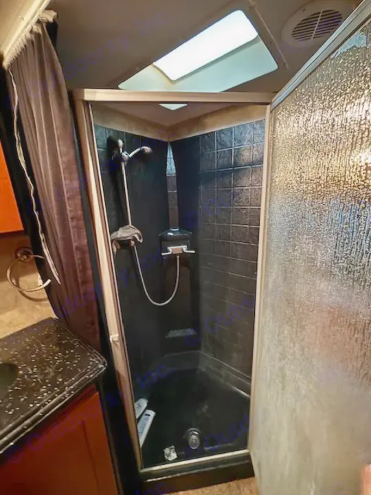 Compact RV rental shower: dark-tiled interior, textured glass door, and a skylight. Practical for on-the-go living.. Keystone RV Fuzion Toy Hauler 2009