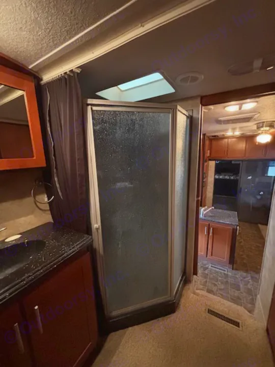 View inside an **RV rental**, showcasing a modern bathroom with a dark vanity, sink, and glass shower enclosure, plus a skylight.. Keystone RV Fuzion Toy Hauler 2009