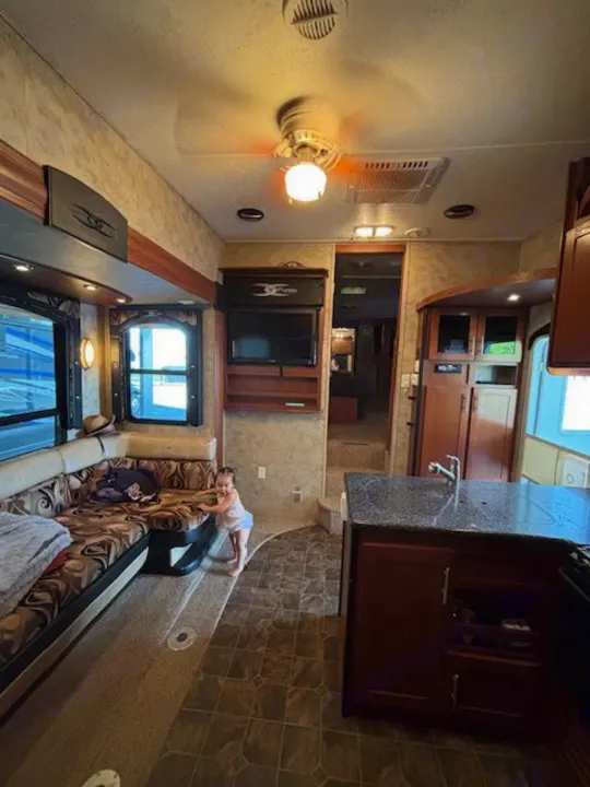 Experience our RV rental's spacious interior: comfy living area, full kitchen, and happy child at play.. Keystone RV Fuzion Toy Hauler 2009
