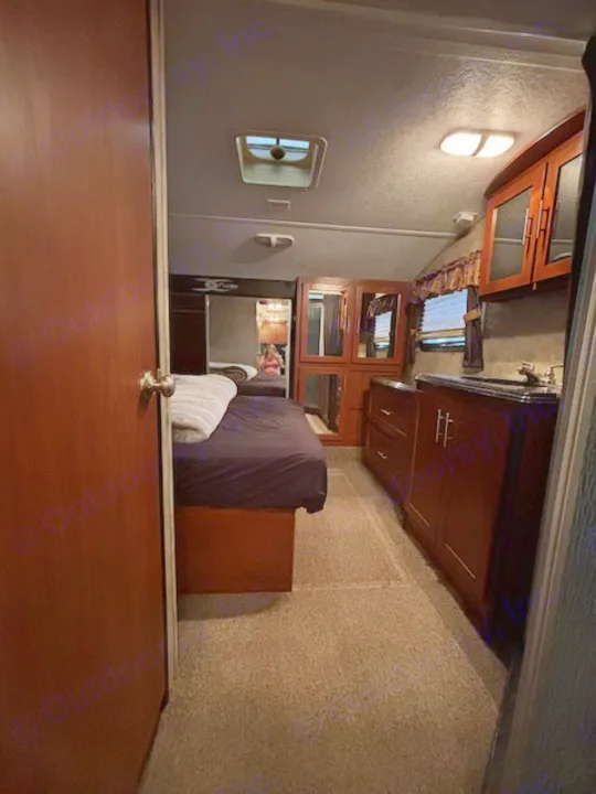 RV rental interior view: a cozy bedroom with a bed on the left, leading to a functional kitchenette with dark wood cabinets and sink on the right.. Keystone RV Fuzion Toy Hauler 2009