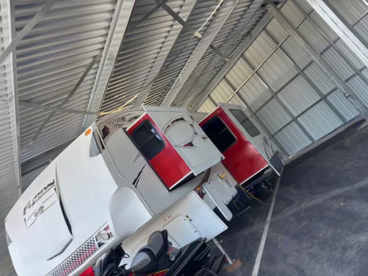 White and red travel trailer with slide-outs extended, stored indoors under a metal roof. Perfect for your next RV rental!. Keystone RV Fuzion Toy Hauler 2009