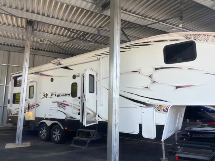 A large white fifth-wheel RV, potentially for rv rental, stored securely under a corrugated metal roof.. Keystone RV Fuzion Toy Hauler 2009