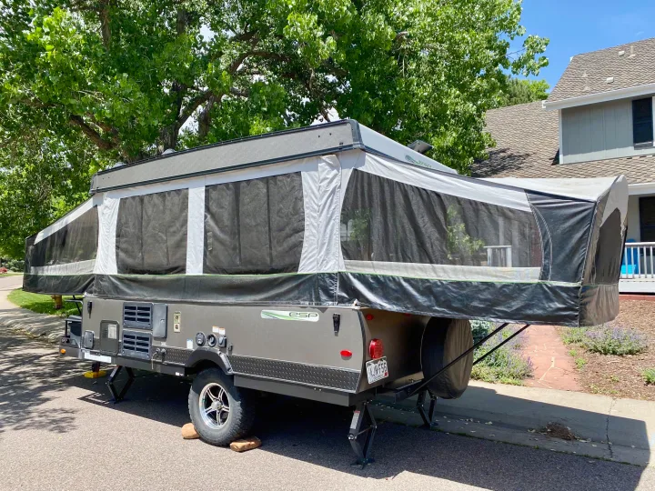 A sleek gray pop-up rv rental, expanded & stabilized, sits on a sunny street next to trees & a house.. Forest River Rockwood ESP 2018