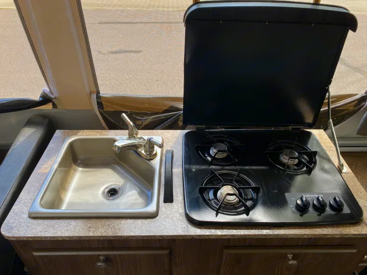 RV rental kitchen: stainless steel sink, faucet, & 3-burner gas stove (Suburban brand) with open lid, inside a pop-up camper.. Forest River Rockwood ESP 2018