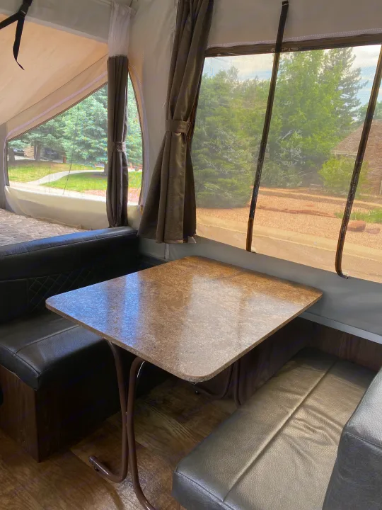 Cozy RV rental dinette setup with a speckled table and dark benches, offering scenic outdoor views through screened windows.. Forest River Rockwood ESP 2018
