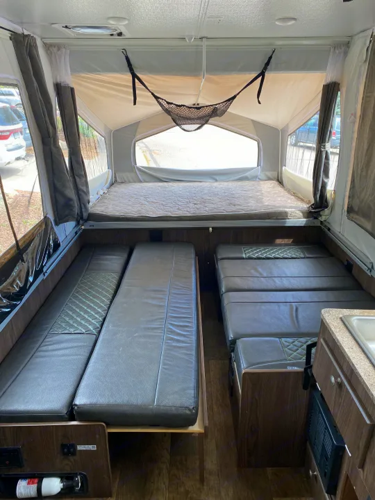 Inside an rv rental: a pop-up camper with a cozy main bed, convertible seating/beds, and a small kitchen sink.. Forest River Rockwood ESP 2018