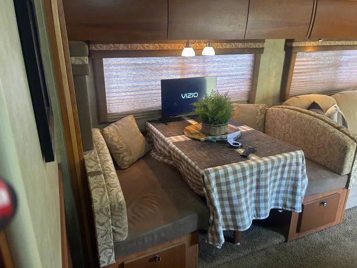 Cozy RV rental dining area with booth seating, table, and TV, offering a functional and compact living space.. Winnebago Sightseer 2009
