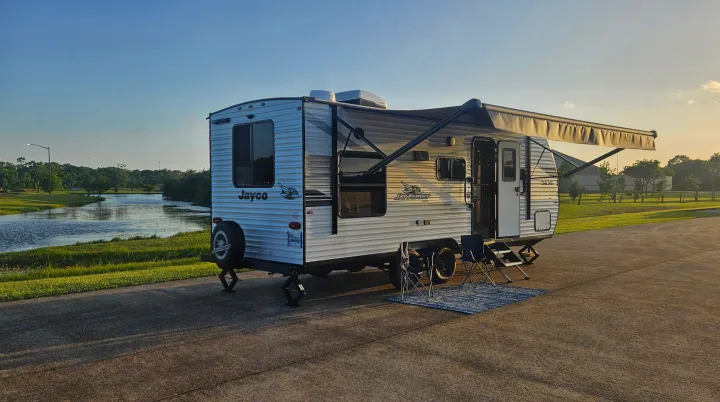 Experience nature with this Jayco RV rental! Travel trailer, awning, chairs, and rug set up by a scenic lake.. Jayco Jay Flight SLX 210 QB 2025