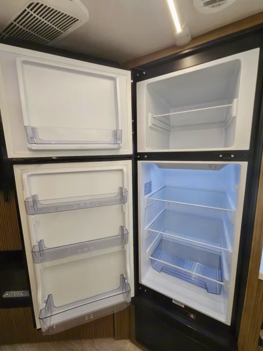 Open, empty two-door refrigerator/freezer unit with clear shelving, ready for your rv rental adventure.. Forest River 26Ice 2025